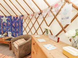 A seating area with an armchair next to a wooden table and a chest of drawers with coasters and flowers at Stardust in Ventnor