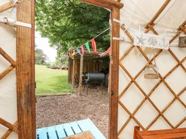 View from inside a yurt looking out to a grassy yard with a wooden shelter decorated with colorful bunting and a barbecue grill at Stardust in Ventnor