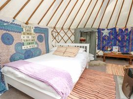 A bed with pillows and a blanket inside a yurt decorated with tapestries rugs a small table and a clothes rack at Stardust in Ventnor