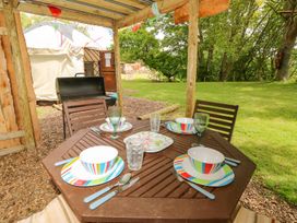 An outdoor dining table set with colorful plates and bowls under a wooden shelter near a grill and a tent in a grassy area at Stardust in Ventnor