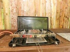 A gas camping stove with three burners on a wooden surface with wooden logs in the background at Stardust in Ventnor