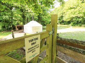 A wooden gate with a sign and a white yurt in a grassy area surrounded by trees at Stardust in Ventnor