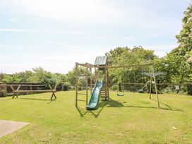 An outdoor playground with a slide a swing and climbing frame on grass with trees behind at Stardust in Ventnor