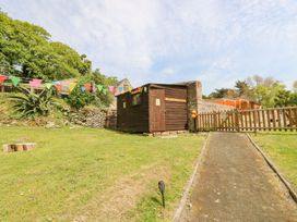 A grassy yard with a small wooden shed marked washrooms a stone wall and a wooden fence with a gate and colorful bunting above in an outdoor setting at Stardust in Ventnor