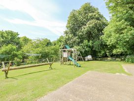A grassy outdoor area with a wooden play structure including a slide and swings surrounded by trees at Stardust in Ventnor