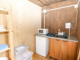 A small kitchenette with wooden cabinets a white mini fridge microwave sink and wooden shelving with towels and plastic storage boxes at Stardust in Ventnor