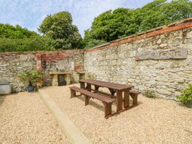 An outdoor patio area with a wooden picnic table and benches stone walls and a barbeque grill at Stardust in Ventnor