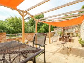 An outdoor patio with metal and wooden chairs a wooden pergola with orange shade cloth and a brick wall at Stardust in Ventnor