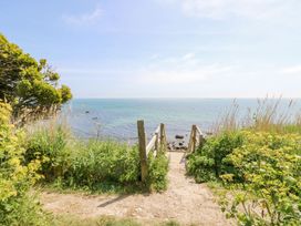 A wooden staircase leading down to a rocky shoreline with green plants and a tree near the path at Stardust in Ventnor