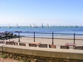 Wooden chairs and tables on a terrace overlooking a sandy beach with sailboats on the sea at Stardust in Ventnor