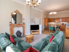 A living room with green sofas red cushions a wooden fireplace a television and a dining area with wooden cabinets at Flat 2 The Old Chapel Whitby