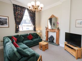 A living room with green sofas and red cushions a wooden fireplace mirror a television on a wooden stand and floral curtains at Flat 2 The Old Chapel in Whitby