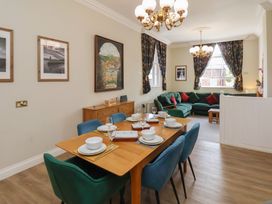 A dining area with a wooden table set for six and a living room with a green sectional sofa and patterned curtains at Flat 2 The Old Chapel in Whitby