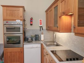 A kitchen with wooden cabinets a double oven a dishwasher a sink a stovetop a kettle and a fire extinguisher at Flat 2 The Old Chapel in Whitby