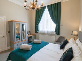 A bedroom with a double bed blue throw pillows green curtains wardrobe dressing table and chandelier at Flat 2 The Old Chapel in Whitby