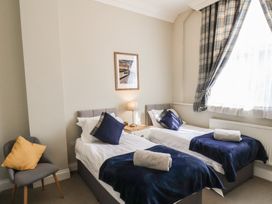 A bedroom with two single beds with blue throws and pillows a chair with a yellow cushion and a window with plaid curtains at Flat 2 The Old Chapel in Whitby