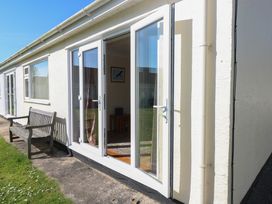 A building exterior with open glass doors next to a wooden bench and grass at Kites - 52 Gower Holiday Village in Scurlage near Port Eynon and Rhossili