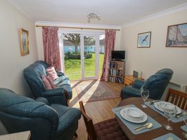 A living room with blue leather sofas a small TV on a bookshelf and a dining table set with plates and glasses at Kites - 52 Gower Holiday Village Scurlage near Port Eynon and Rhossili