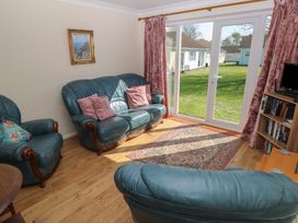 A living room with blue leather sofas pink cushions a rug and a TV near large sliding glass doors at Kites - 52 Gower Holiday Village Scurlage near Port Eynon and Rhossili