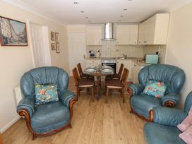 A dining area with a wooden table set for four and a kitchen with white cabinets and appliances and two blue leather armchairs with floral cushions