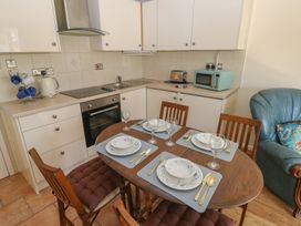 A kitchen and dining area with a wooden table set for four and white cabinets with appliances at Kites - 52 Gower Holiday Village Scurlage near Port Eynon and Rhossili