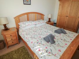 A bedroom with a wooden bed with floral bedding two bedside tables with lamps and a wooden wardrobe at Kites - 52 Gower Holiday Village Scurlage near Port Eynon and Rhossili