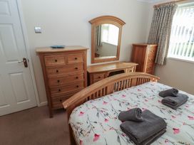 A bedroom with a wooden bed, dresser, mirror, chest of drawers, and folded towels on the bed at Kites - 52 Gower Holiday Village Scurlage near Port Eynon and Rhossili