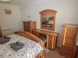 A bedroom with wooden furniture including a bed, dressing table with a mirror, two chests of drawers, and towels on the bed at Kites - 52 Gower Holiday Village in Scurlage near Port Eynon and Rhossili