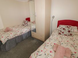 A bedroom with two single beds with floral bedding a wardrobe and a floor lamp at Kites - 52 Gower Holiday Village in Scurlage near Port Eynon and Rhossili