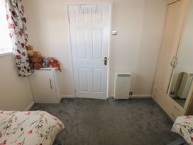 A bedroom with a bed with floral bedding a white door a cabinet with stuffed animals and a wardrobe with mirrored doors at Kites - 52 Gower Holiday Village Scurlage near Port Eynon and Rhossili