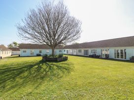 A large tree with a circular stone bench around it on a grassy courtyard surrounded by single-story buildings at Kites - 52 Gower Holiday Village in Scurlage near Port Eynon and Rhossili