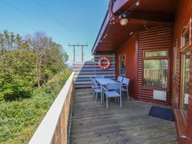A wooden balcony with a white table and six chairs and a life ring on a wall at The Beach House in Watermouth near Combe Martin
