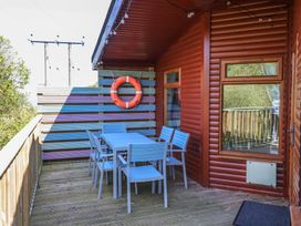 An outdoor wooden deck with a blue dining table and chairs and a lifebuoy on a wooden fence at The Beach House in Watermouth near Combe Martin