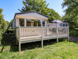 A caravan with a wooden deck and outdoor table with umbrella surrounded by trees at Caravan 941 in Clacton-On-Sea