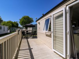 An outdoor deck area with a table and chairs under an umbrella attached to a beige caravan at Caravan 941 in Clacton-On-Sea