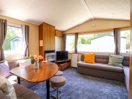 A living area with a wooden dining table flowers on a table gray sofas with cushions and a television at Caravan 941 in Clacton-On-Sea