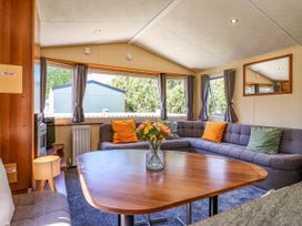 A living area with a wooden table with flowers and an L-shaped sofa with cushions in Caravan 941 in Clacton-On-Sea