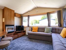 A living room with a corner sofa with cushions a wooden table with stools a TV on a wooden stand and a fireplace at Caravan 941 in Clacton-On-Sea