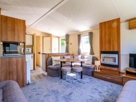 A living area with a round dining table and cushioned seating a fireplace and windows with curtains at Caravan 941 in Clacton-On-Sea