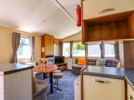A living area with a dining table set, two sofas with cushions, a television, and curtains on windows at Caravan 941 in Clacton-On-Sea