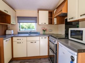 A kitchen with cream cabinets a gray countertop a window with a blind a stove a microwave a refrigerator a toaster and a vase with flowers at Caravan 941 in Clacton-On-Sea