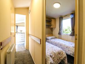 A hallway with a radiator leading to a kitchen and a bedroom with two single beds and a window with curtains at Caravan 941 in Clacton-On-Sea