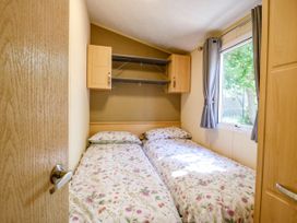 A bedroom with two single beds with floral bedspreads a window with grey curtains and wooden cabinets at Caravan 941 in Clacton-On-Sea