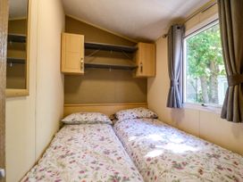 A bedroom with two single beds floral bedding cabinets and a window with curtains at Caravan 941 in Clacton-On-Sea