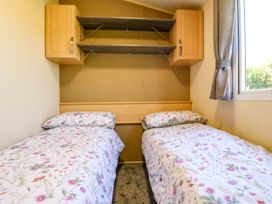 A bedroom with two single beds floral bedcovers wooden cabinets and shelves and a window with curtains at Caravan 941 in Clacton-On-Sea