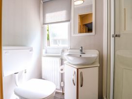 A bathroom with a toilet, sink with cabinet, mirror, radiator, window with blind and shower enclosure at Caravan 941 in Clacton-On-Sea