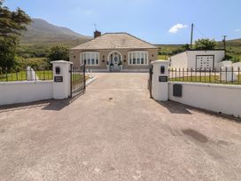 A bungalow house with a driveway and gated entrance set against a mountain backdrop at Killelton Cottage in Camp County Kerry