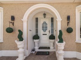 Front door entrance with white door under an archway flanked by potted topiary plants and hanging round greenery at Killelton Cottage Camp County Kerry