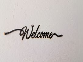 A black metal welcome sign mounted on a white textured wall at Killelton Cottage in Camp County Kerry