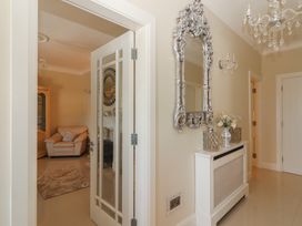 A hallway with a decorative silver-framed mirror above a white radiator cover and a view into a living room with a beige armchair and a cabinet at Killelton Cottage in Camp County Kerry